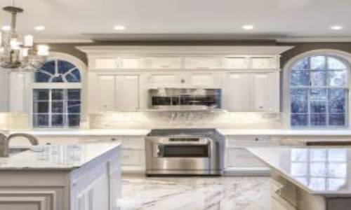 Indoor photo of a beautifully decorated large kitchen, dark marble floors, luxurious kitchen in an extravagant home, long granite and wood island, kitchen sink, refrigerator, barstools, white, silver, deep browns, gold colour theme.