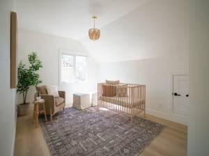 Bright minimalist baby nursery with wooden crib, chair and soft rug in modern residential home representing family living, home ownership and real estate concepts.